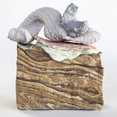 a sculpture by Lily Cox-Richard of plaster casts of tree bark, a sweater sleeve and part of a basket, all stacked on top of a piece of sandstone